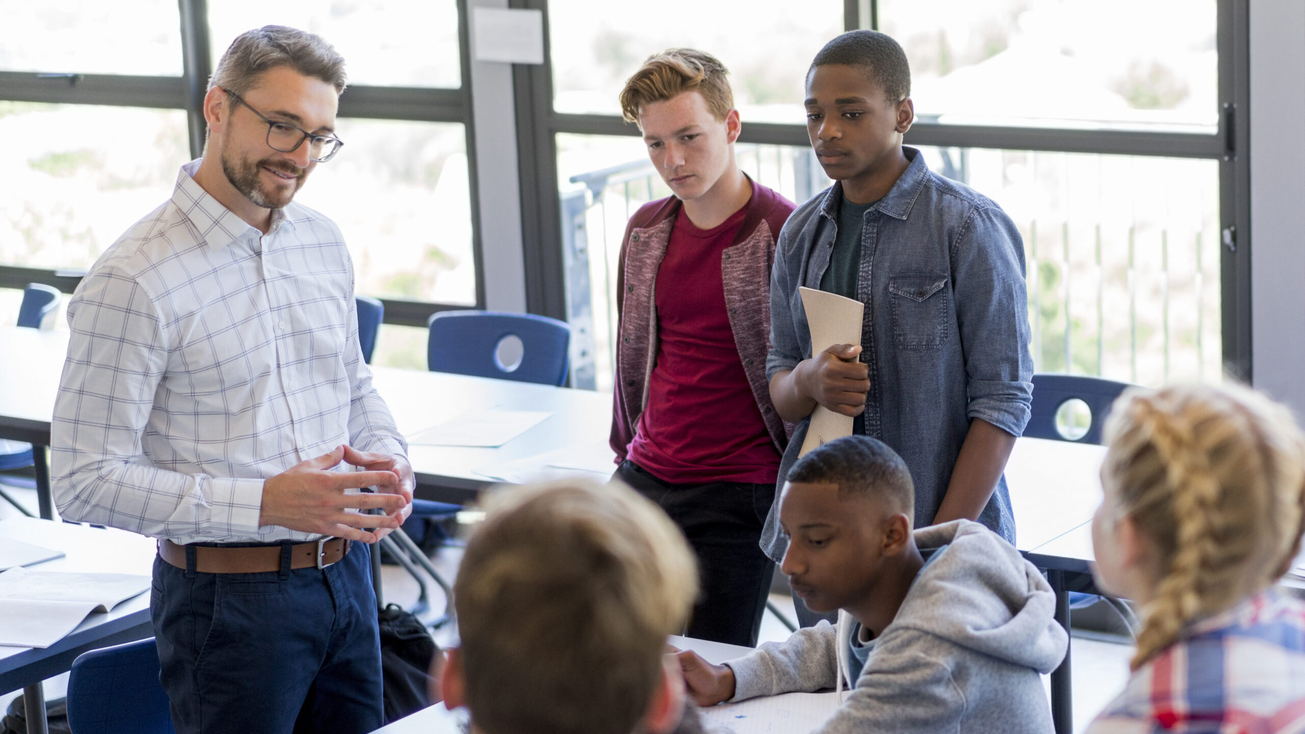 High angle view of professor is teaching in classroom. Multi-ethnic students and male teacher are discussing at school. They are wearing casuals in high school building.