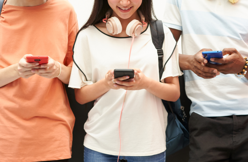 Three students standing next to each other holding cell phones in their hands.