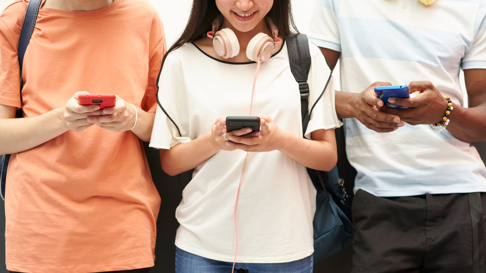 Three students standing next to each other holding cell phones in their hands.